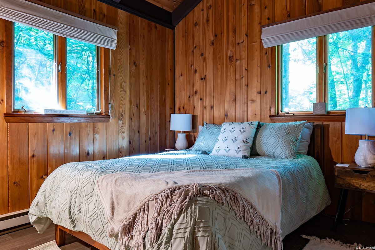 Queen bed in a wood-paneled bedroom overlooking the trees